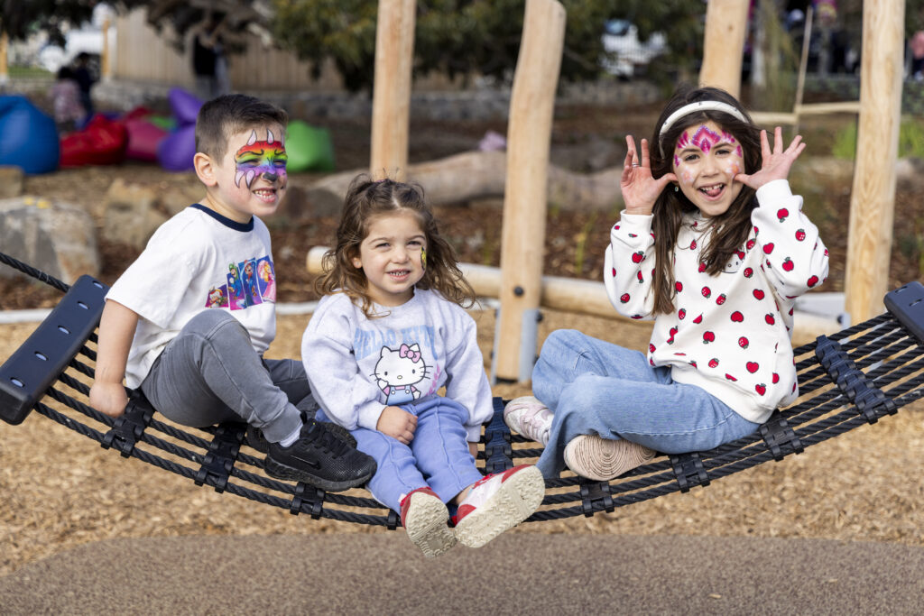 Three children with face paint on playground swing